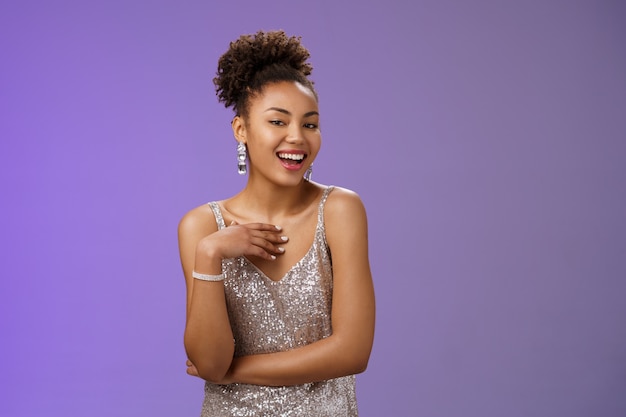 Foto elegante mujer milenaria con estilo afroamericano atractivo descarado en brillante elegante vestido plateado alardeando de novia chismosa durante la fiesta disfrutando de divertirse en el club nocturno, fondo azul.