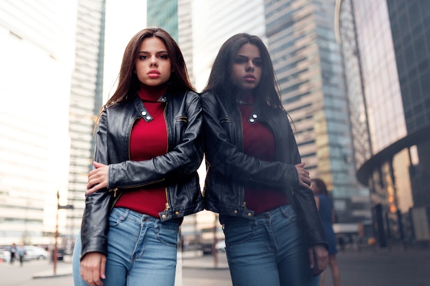 Elegante mujer moderna con cabello alisado en un suéter rojo de moda, chaqueta de cuero negro y jeans azul posando en la calle