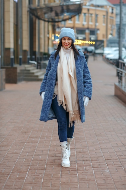 Elegante mujer morena en abrigo caminando en la ciudad en invierno