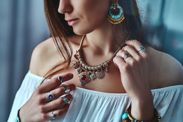 Elegante mujer morena boho con blusa blanca con grandes aretes, collar con  piedra y anillos de plata. traje bohemio gitano hippie indio de moda con  detalles de bisutería