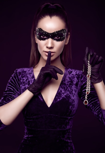 Elegante mujer morena con hermoso vestido morado, máscara de lentejuelas y guantes negros