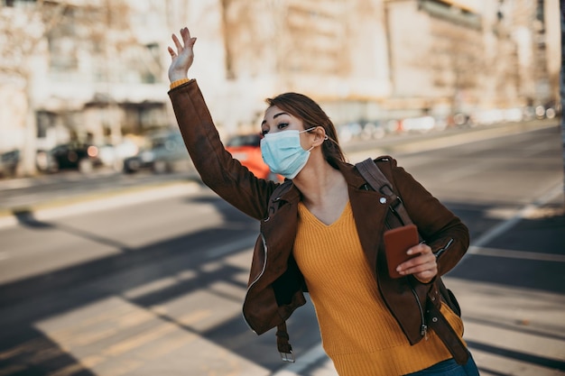 Foto elegante mujer de negocios con máscara protectora parada sola en una calle vacía y esperando el transporte en autobús o taxi. concepto de estilo de vida del virus corona o covid-19.