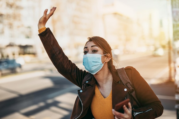 Foto elegante mujer de negocios con máscara protectora parada sola en una calle vacía y esperando el transporte en autobús o taxi. concepto de estilo de vida del virus corona o covid-19.