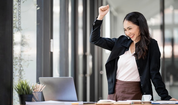 Elegante mujer de negocios de pie en la oficina con tableta digital Emocionada mujer de negocios asiática levantando la mano para felicitar mientras trabaja en una computadora portátil en la oficinax9