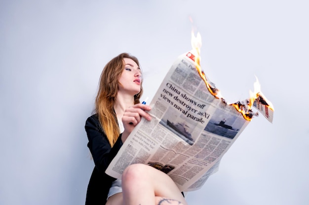 Una elegante mujer de negocios rubia fumando y sosteniendo un periódico encendido en el estudio