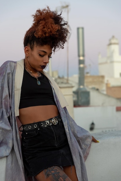 Elegante mujer negra con cabello rizado y vistiendo un kimono lila y mirando hacia abajo en la terraza en Cádiz España