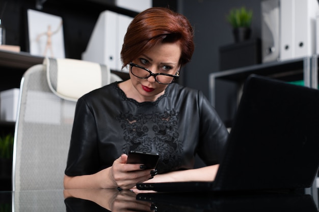 Elegante mujer que trabaja con ordenador portátil y teléfono en la oficina