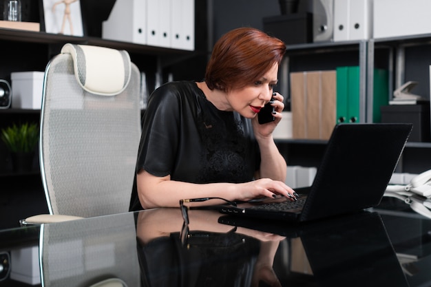 Elegante mujer que trabaja con ordenador portátil y teléfono en la oficina