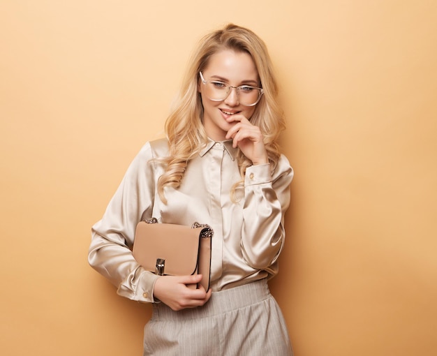 Elegante mujer rubia en blusa y pantalones posando sobre fondo beige