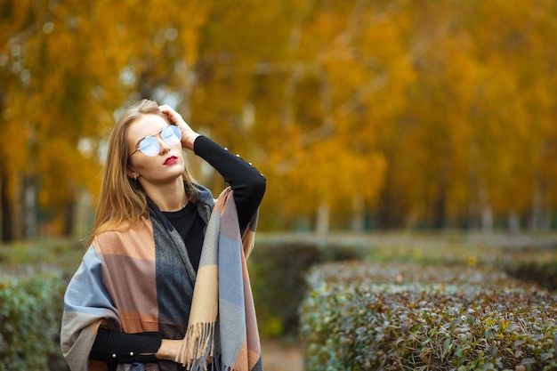 Foto elegante mujer rubia de pelo largo con suéter, bufanda y gafas. espacio vacio