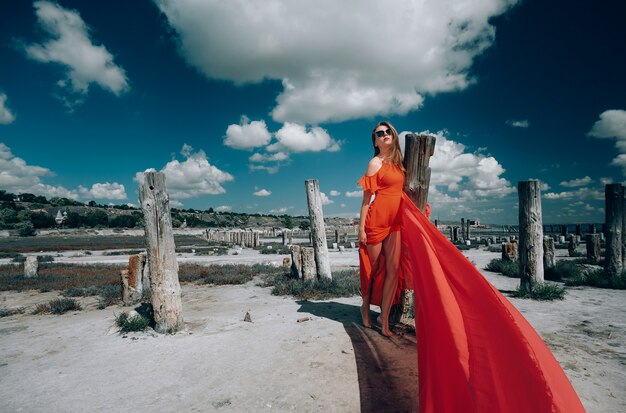 Elegante mujer rubia con vestido rojo en la playa