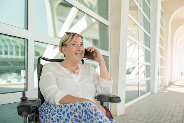 Una elegante mujer sonriente sentada en una silla de ruedas hablando por teléfono inteligente