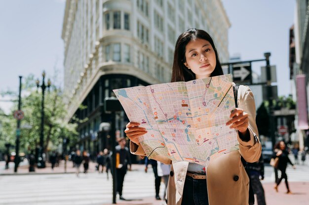 elegante mujer turista viaja sola en vacaciones de primavera a san francisco sosteniendo un mapa de papel buscando la dirección de la famosa atracción. edificio plano blanco en el fondo bajo la luz del sol en verano.