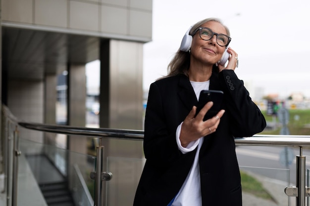 Elegante mulher adulta caucasiana madura ouvindo música com fones de ouvido com um telefone em