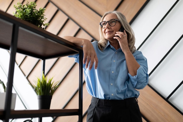 Elegante mulher adulta de negócios falando ao telefone no escritório