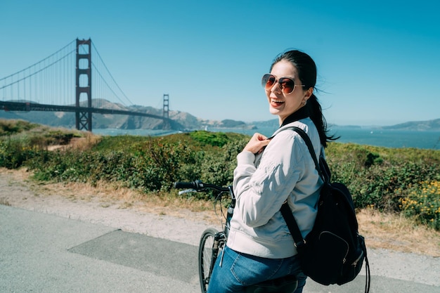 elegante mulher chinesa viajando de bicicleta está se virando para olhar para a câmera com um sorriso perto da ponte golden gate em San Francisco Califórnia EUA no verão.