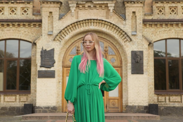 Elegante mulher de cabelo rosa vestindo vestido verde em frente a um belo prédio antigo