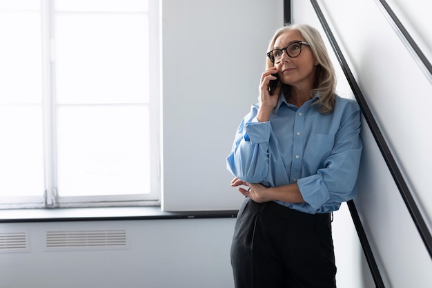 Elegante mulher de negócios caucasiana madura em uma camisa azul fala em um telefone celular no escritório