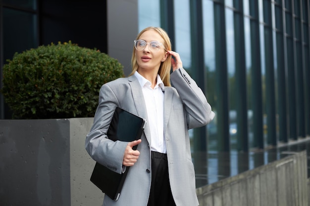 Elegante mulher de negócios usando óculos segurando o cabelo correto do laptop andando na rua