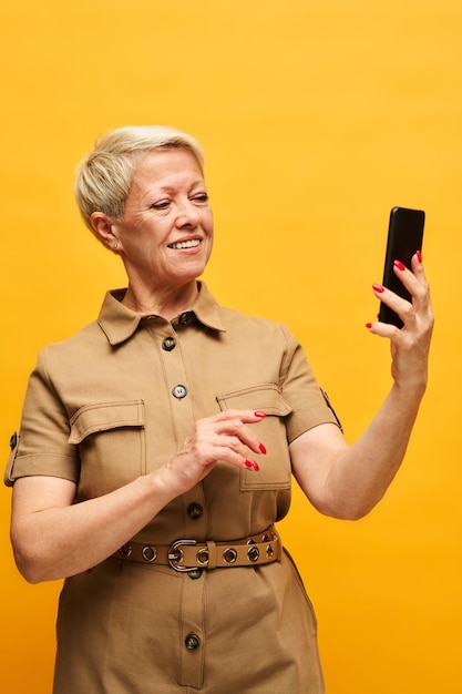 Elegante mulher loira madura em curativo de dopamina usando smartphone