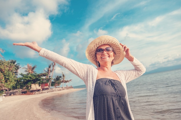 Foto elegante mulher madura atraente 50-60 com os braços abertos à beira-mar, viagens e aposentadoria, moda e beleza, idosos ativos