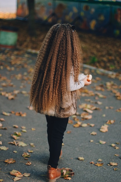 Elegante niña de 4-5 años con botas, abrigo de piel con pelo muy largo y rizado. Vista desde atrás. Otoño temporada de otoño