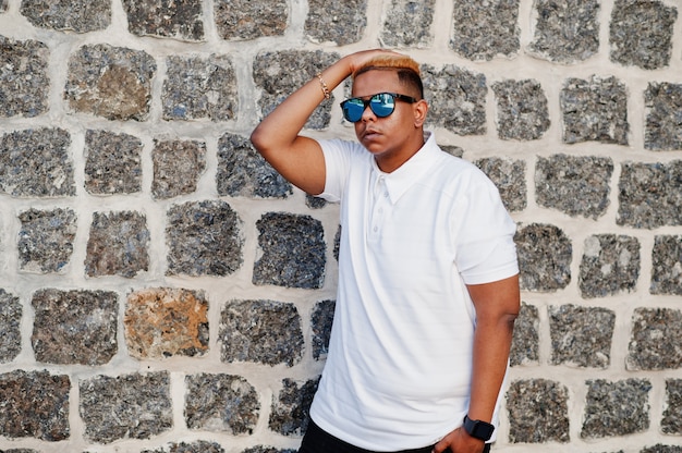 Elegante niño musulmán árabe con originalmente cabello y gafas de sol en las calles contra la pared de ladrillo.