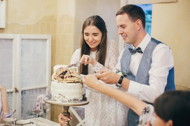 Elegante noiva e noivo cortando bolo moderno com lavanda no fundo da mesa festiva no elegante restaurante Provence recepção de casamento Lindo casal de noivos comemorando
