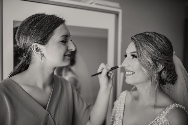 Elegante noiva feliz vestindo vestido sorrindo para damas de honra na janela casamento rústico preparação matinal nupcial se preparando momento emocional espaço para texto preto branco foto