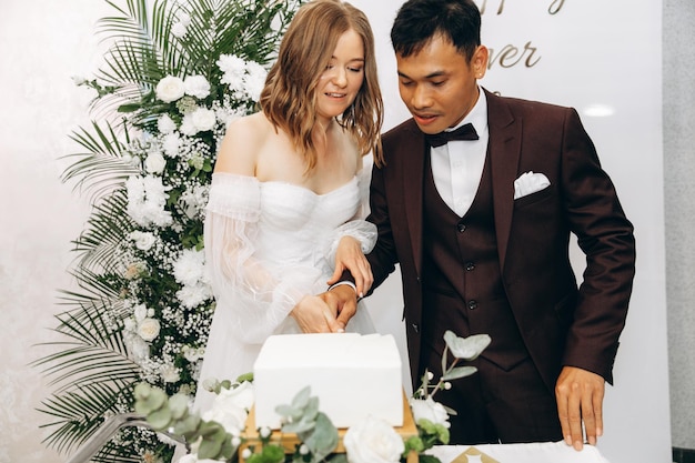 Elegante novia bonita y novio asiático comiendo pastel de bodas