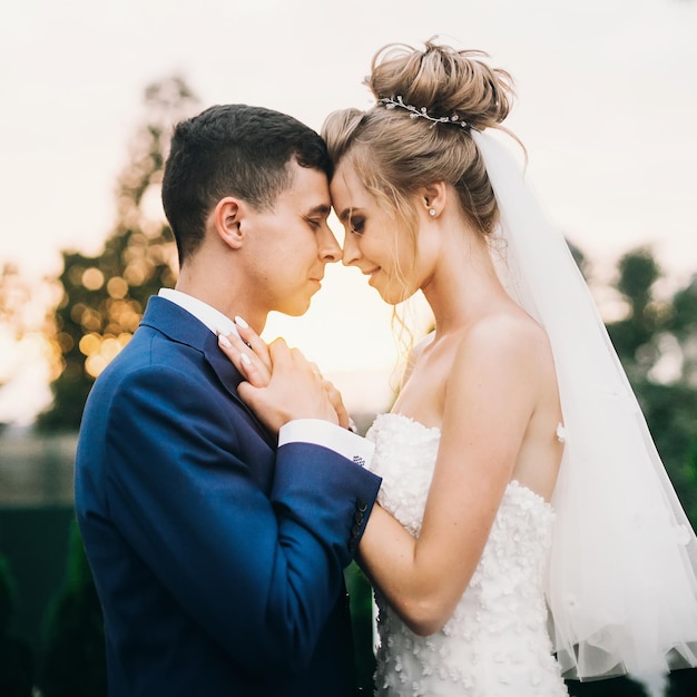 Elegante novia feliz y el novio posando en la cálida luz del atardecer en la recepción de la boda al aire libre