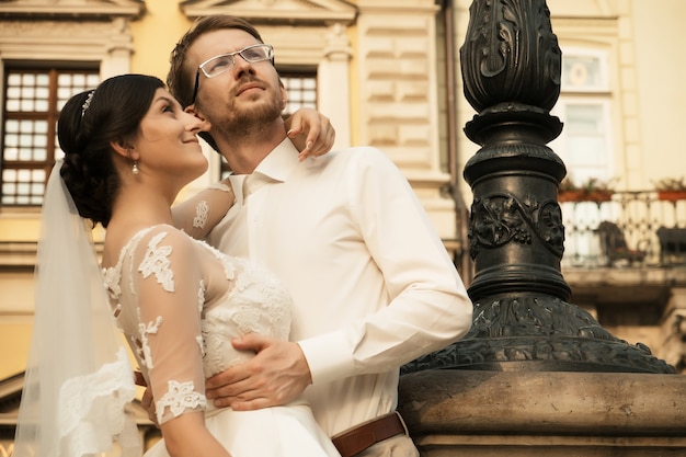 Elegante novia de lujo y elegante novio, abrazándose con ternura, en el fondo de la ciudad vieja de Lviv