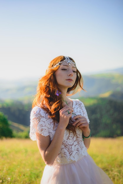 Elegante novia de pie en el hermoso paisaje de montañas al atardecer