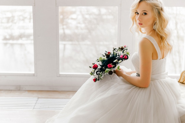 Elegante novia rubia en vestido de novia hermoso con boquet de flores decorativas brillante retrato de estudio.