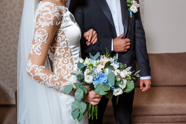 Elegante novia en un vestido de novia con encaje y novio en traje negro sosteniendo en las manos ramo de flores de novia