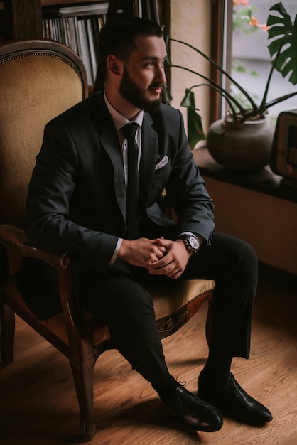 Elegante novio sentado en la silla en la biblioteca