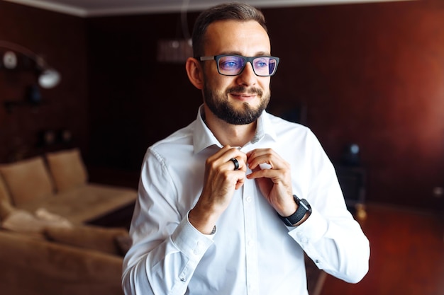 Elegante novio vistiéndose y preparándose para la boda abrocha botones en la camisa