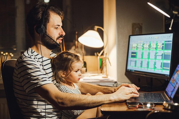 Elegante padre barbudo trabajando en casa mientras cuida a su hija juguetona