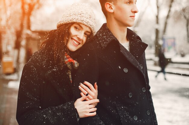 elegante pareja amorosa en abrigos negros caminando en la ciudad de nieve de invierno