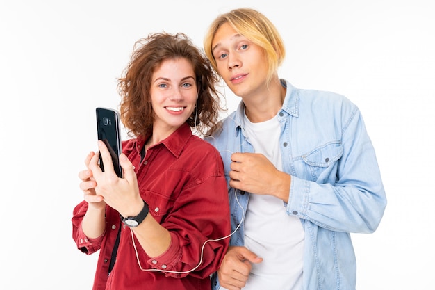 Elegante pareja caucásica enamorada escuchar música y hacer selfie aislado en la pared blanca