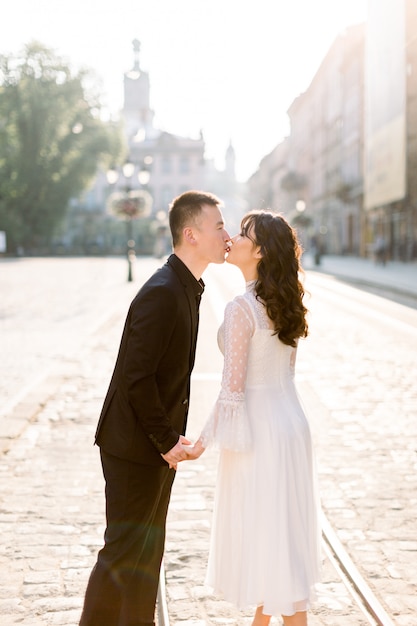 Elegante pareja hermosa recién casados asiáticos caminando por las calles de la ciudad vieja, besándose, en un día soleado de su boda