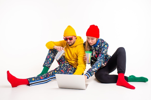Elegante pareja de hombre y mujer en ropa colorida mirando la pantalla del portátil sobre la pared blanca