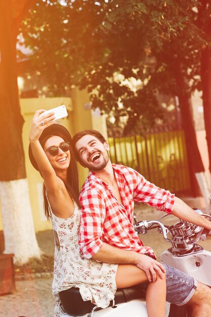 Elegante pareja joven feliz haciendo autofoto en scooter