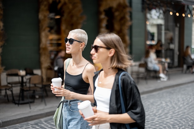 Elegante pareja de mujeres de pie junto con tazas de café al aire libre