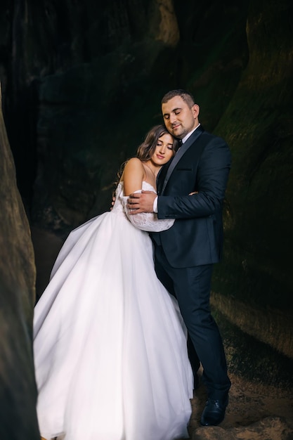 Elegante pareja de recién casados se encuentra entre las rocas abrazándose