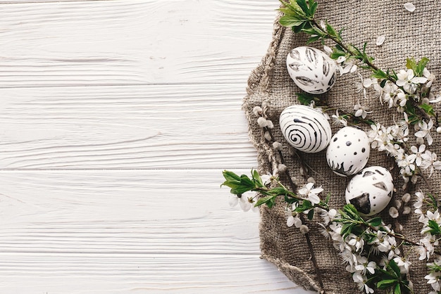 Elegante piso de pascua con huevos pintados en colores blanco y negro en un fondo rústico de madera con flores de primavera feliz espacio de tarjeta de felicitación de pascua para texto huevos de pascua modernos