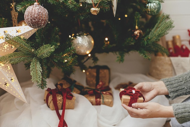Elegante presente de natal em mãos sob a árvore de natal com luzes feliz natal boas festas