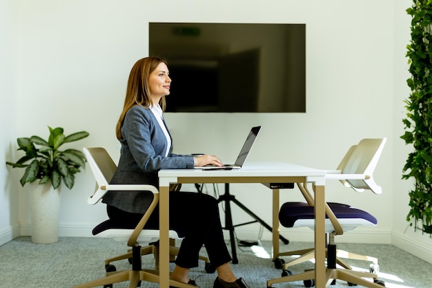 Foto elegante professionelle frau lächelt, während sie an einem laptop in einem hellen büro arbeitet