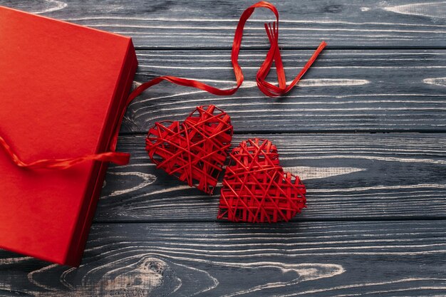 Elegante regalo rojo y dos cintas de corazón planas sobre fondo negro de madera rústica feliz día de san valentín concepto tarjeta de felicitación con espacio para texto