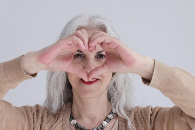 Elegante reife Frau mit grauem Haar macht Form des Herzens mit den Fingern positive Damenausdrücke